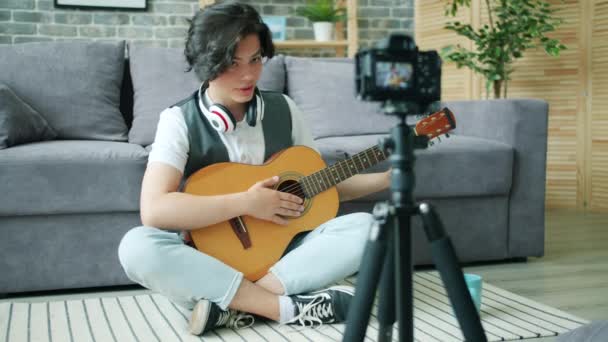 自宅でギターを保持するインターネットブログのための十代のギタリストのレコーディングビデオ — ストック動画