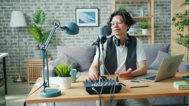 Щасливий підліток розмовляє в мікрофоні за допомогою звукового мікшера в студійному записі подкасту — стокове відео