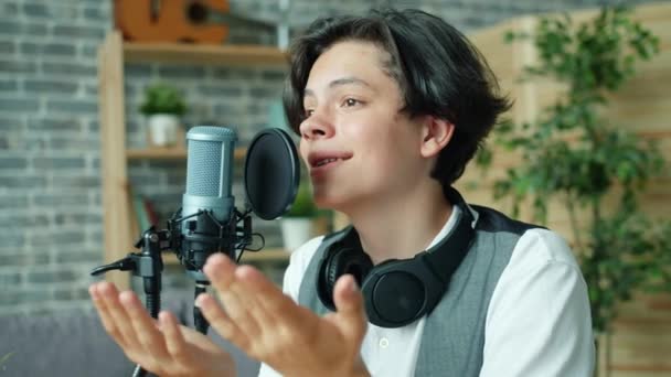 Portrait d'un adolescent souriant parlant en micro dans un studio d'enregistrement sonore seul — Video