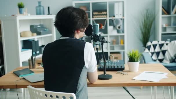 Back view of teenager recording audio podcast in studio talking in microphone — Stock Video