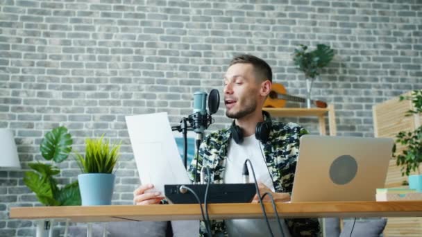 Alegre chico leyendo en micrófono celebración de papel haciendo podcast en estudio — Vídeo de stock