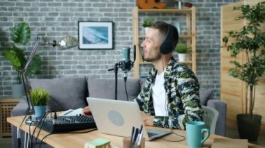 Stüdyoda dizüstü bilgisayar kullanarak kulaklık takan mikrofon konuşan neşeli adam