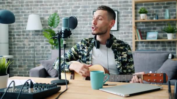 Молодой певец играет на гитаре и поет в подкасте микрофона — стоковое видео