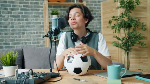 Adolescente feliz hablando en micrófono en estudio de grabación sosteniendo el fútbol — Vídeo de stock