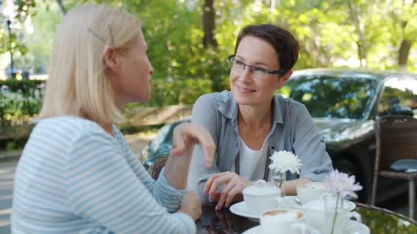 Mulheres adultas atraentes falando em café ao ar livre gesticulando à mesa com bebidas — Vídeo de Stock