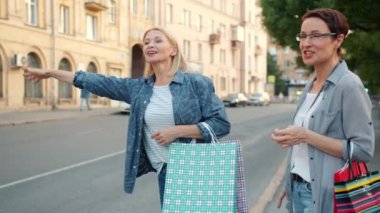 Alışveriş poşetleri ile gülümseyen kadınlar şehir caddesinde el sallayarak taksi selamlıyor