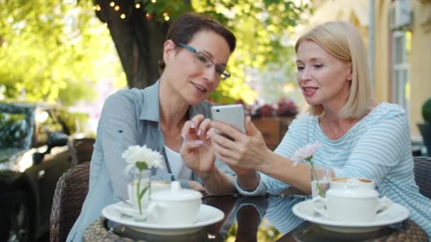 Šťastné dámy se smíchem při pohledu na elegantní telefonní obrazovku v venkovní kavárně — Stock video