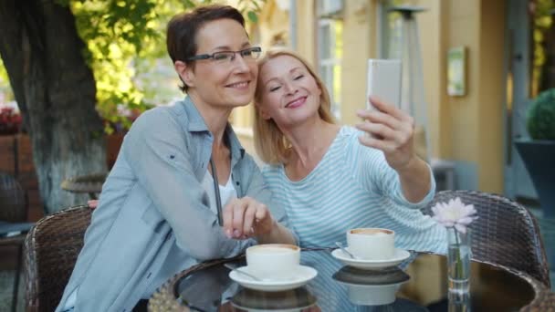 Hermosas mujeres tomando selfie con cámara de teléfono inteligente y hablando en la cafetería al aire libre — Vídeos de Stock