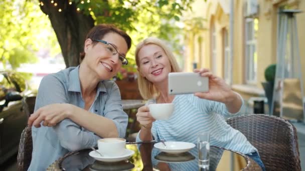 Блондинка делает селфи с другом в кафе, держа кофе, используя смартфон. — стоковое видео