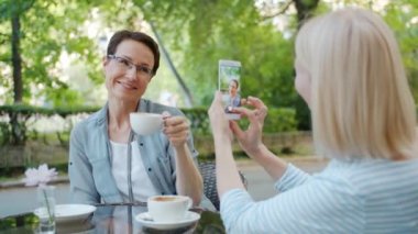 Güzel bayan çay fincan tutan sokak kafede akıllı telefon kamera için poz