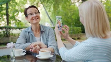 Çekici kadın açık havada kafede akıllı telefon kamerası için poz el sallayarak