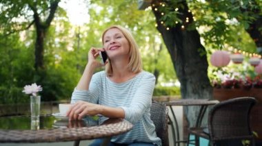 Mutlu olgun kadın sokak kafede otururken gülen cep telefonu konuşuyor