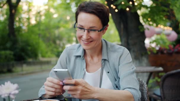 Smiling lady using smartphone touching screen smiling in street cafe outside — Stock Video