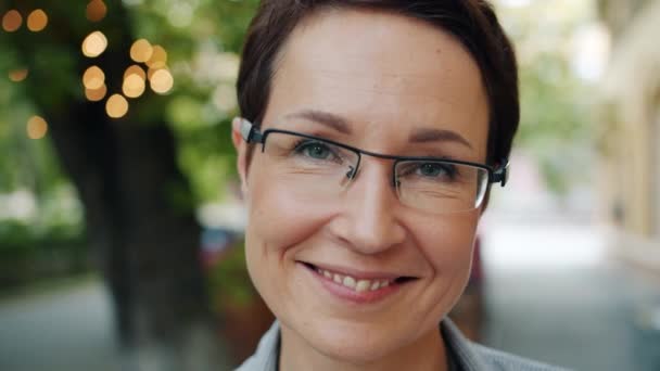 Primer plano retrato de mujer de negocios madura en gafas sonriendo a la cámara al aire libre — Vídeo de stock