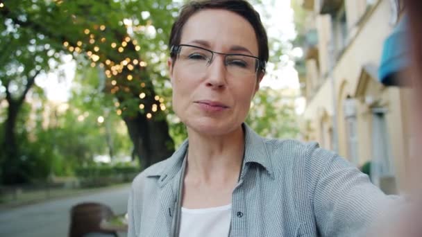 Porträt einer glücklichen Dame, die einen Online-Videoanruf macht und draußen winkt und Kuss sendet — Stockvideo