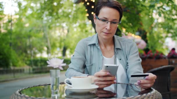Зріла бізнес-леді робить оплату кредитною карткою за допомогою смартфона в кафе — стокове відео