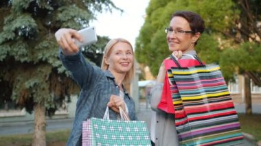 Açık havada alışveriş poşetleriyle poz veren akıllı telefon kamerasıyla selfie çeken kadınlar