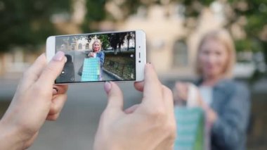 Alışveriş poşetleri ile olgun kadının fotoğrafını çeken akıllı telefon ekranının yakın çekim