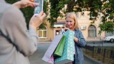 Sokakta alışveriş poşetleri tutan akıllı telefon kamerası için poz güzel sarışın
