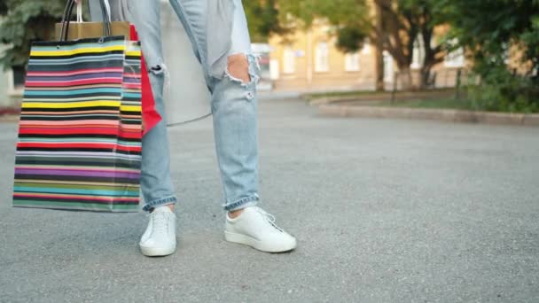 Frau mit trendiger Kleidung und Schuhen, die mit Einkaufstaschen im Freien Fuß fassen — Stockvideo