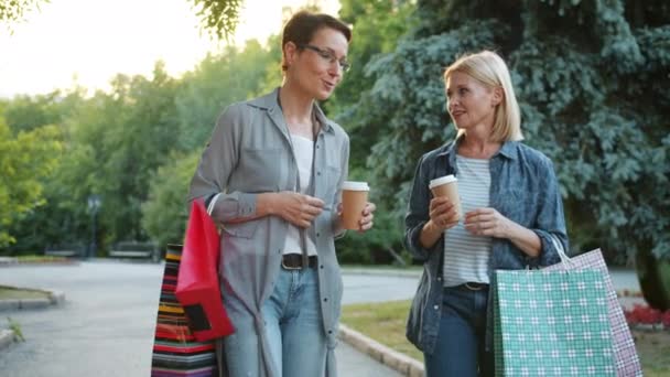 Веселі дами розмовляють у парку з сумками, насолоджуючись вихідними — стокове відео