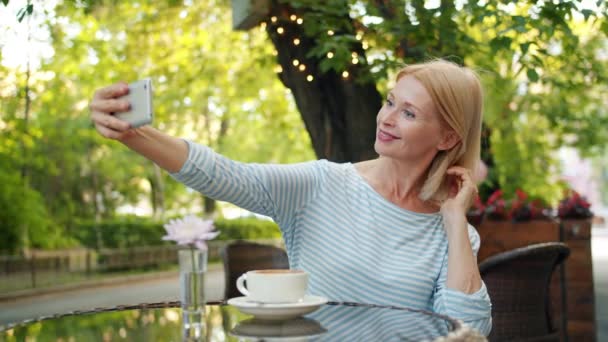 Χαρούμενη Κυρία παίρνοντας selfie με smartphone κάμερα που ποζάρει σε υπαίθριο καφέ μόνο — Αρχείο Βίντεο