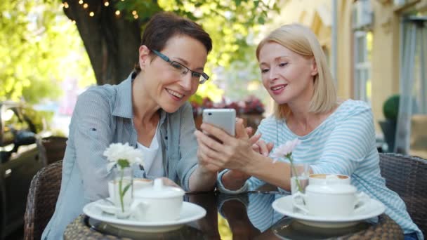 Şehir caddesindeki açık hava kafede gülen akıllı telefonu kullanan heyecanlı kadınlar — Stok video
