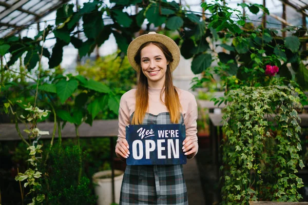 オープンサイン笑顔のバイヤーを歓迎して温室に立っている美しい女性 — ストック写真