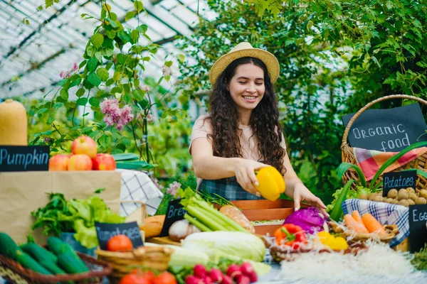 Счастливая женщина фермер в фартуке положить органические продукты на стол на рынке улыбаясь — стоковое фото