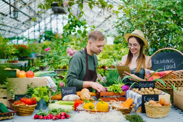 Niña y chico granjeros hablando poniendo comida orgánica en la mesa en la venta de invernadero —  Fotos de Stock