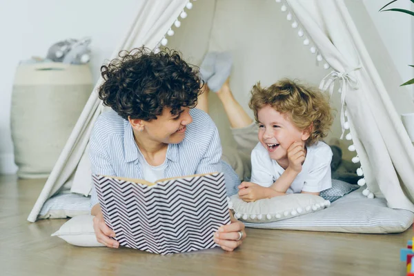 居心地の良いテントの屋内で床に横たわっているかわいい子供に本を読んで愛する母 — ストック写真
