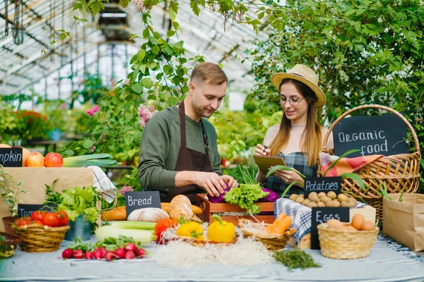 Vrolijke jonge mensen boeren die biologisch eten op tafel zetten bij de verkoop van de boerderij — Stockfoto