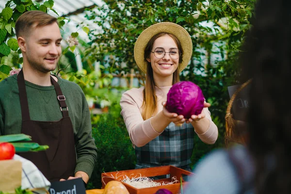 Smiling girl in apron farmer selling cabbage to female customer at autumn sale