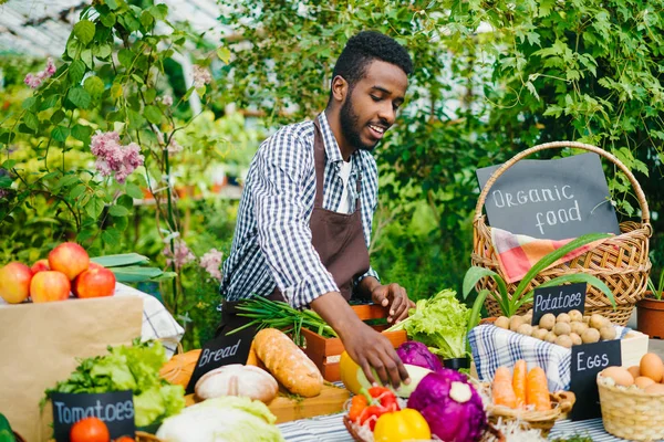 African American sprzedawca oddanie świeżych warzyw organicznych na stole na sprzedaż na farmie — Zdjęcie stockowe