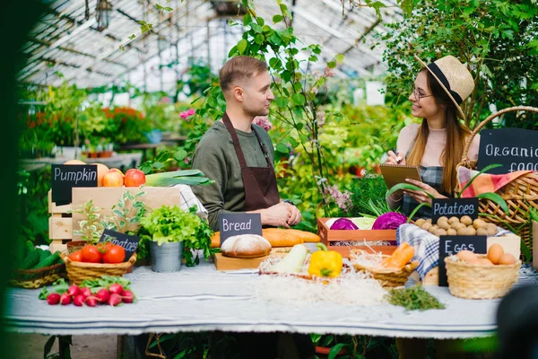 Продаж людей чоловік і жінка розмовляють під час продажу органічної їжі в теплиці — стокове фото
