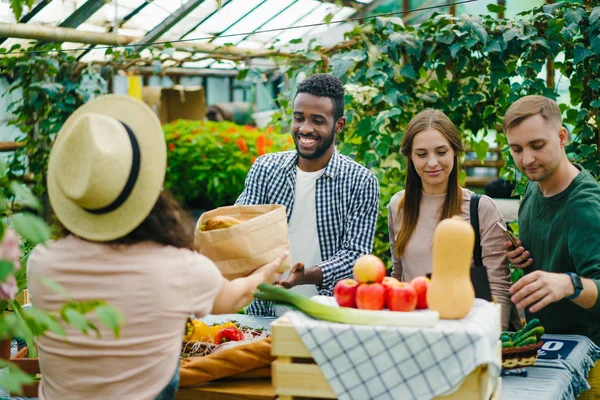 Jovens felizes comprando alimentos orgânicos no mercado conversando com agricultoras — Fotografia de Stock
