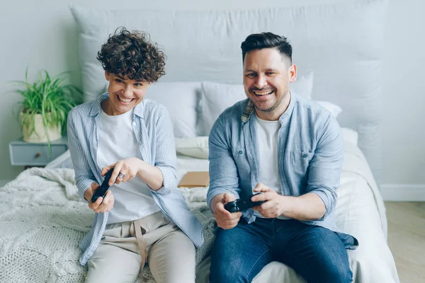 Férfi és nő játszik videójáték ül az ágyban az apartmanban szórakoztunk — Stock Fotó