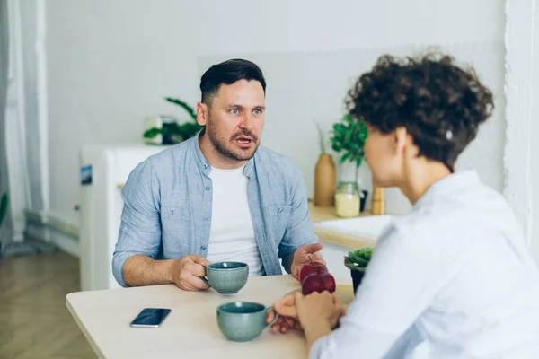 Unglückliches Paar, Mann und Frau, die am Tisch in der Küche sitzen und reden — Stockfoto