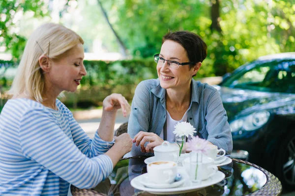 Güzel olgun kadın sokak kafede eğlenerek gülümseyerek arkadaşıyla konuşurken — Stok fotoğraf