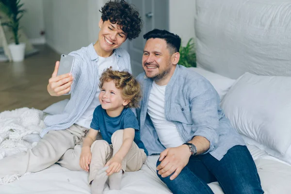 Perfecto chico chica de la familia y el niño tomando selfie en casa en la cama con el teléfono inteligente —  Fotos de Stock