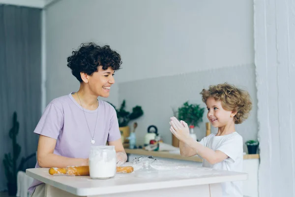 Счастливый ребенок веселится с мукой хлопать в ладоши приготовления выпечки с мамой дома — стоковое фото