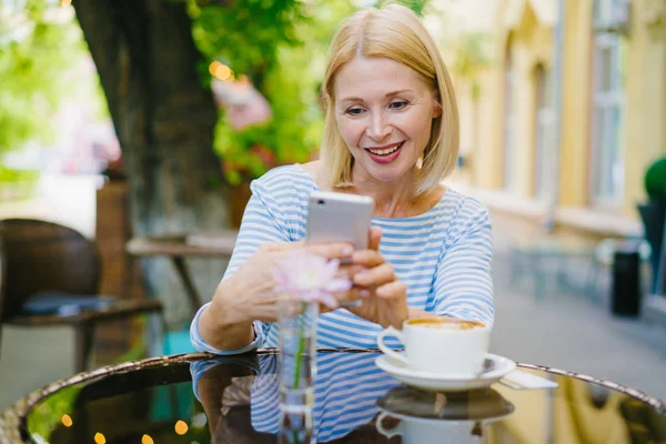 Atraktivní Zralá blondýna používající smartphone užívající letní den v otevřené vzdušné kavárně — Stock fotografie