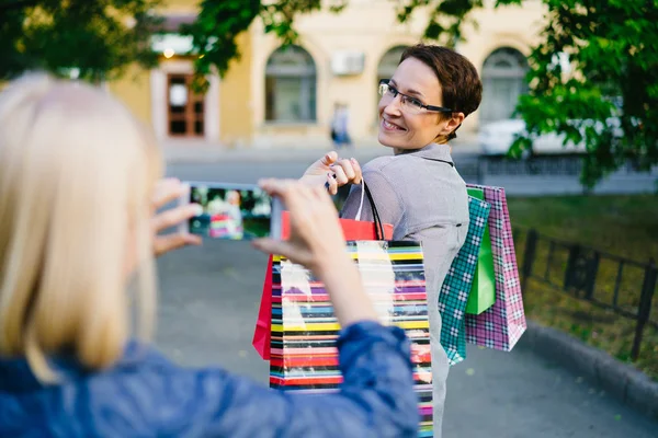 Alışveriş çantaları ile çekici kadın akıllı telefon kamera için poz açık havada — Stok fotoğraf