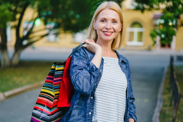 Portrait of good-looking blonde holding shopping bags outdoors in city street — Stock Photo, Image