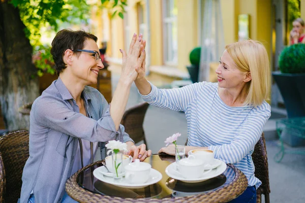 Mutlu kadın arkadaşlar yüksek beş yapıyor ve yaz aylarında açık hava kafede gülüyor — Stok fotoğraf