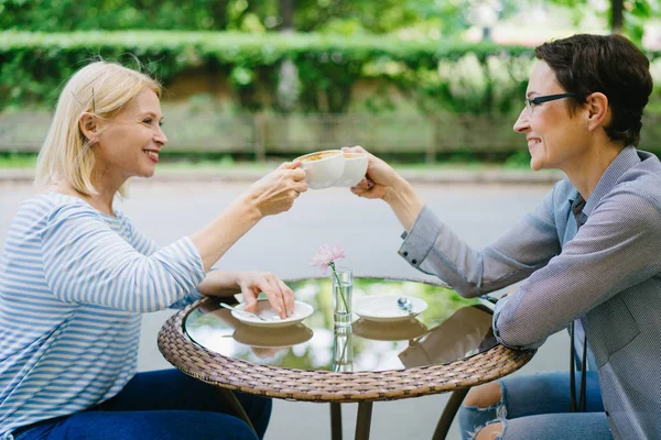 Mujeres felices amigos tazas de café tintineo en la cafetería al aire libre disfrutando del día de verano — Foto de Stock