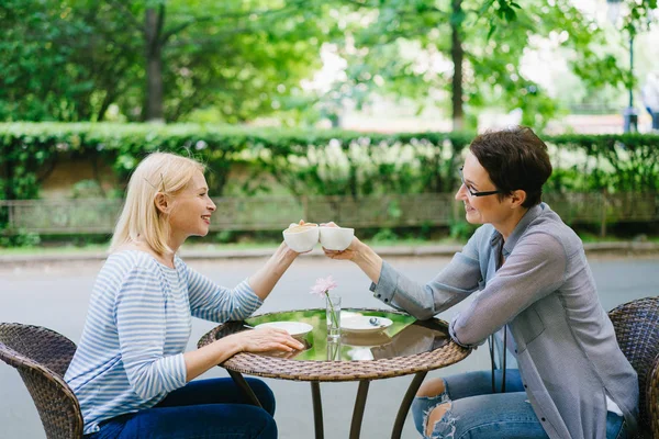 Maduras amigas celebrando reunión tazas de té tintineo en café al aire libre — Foto de Stock
