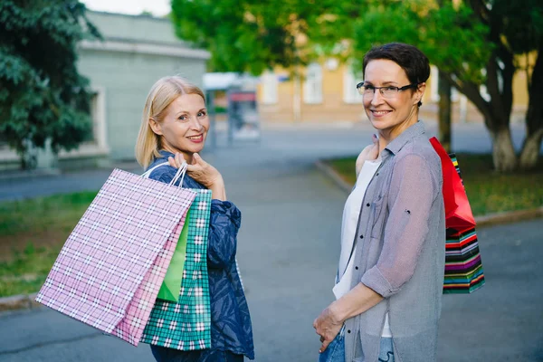 Portrait de dames heureuses marchant à l'extérieur avec des sacs se tournant vers la caméra souriant — Photo