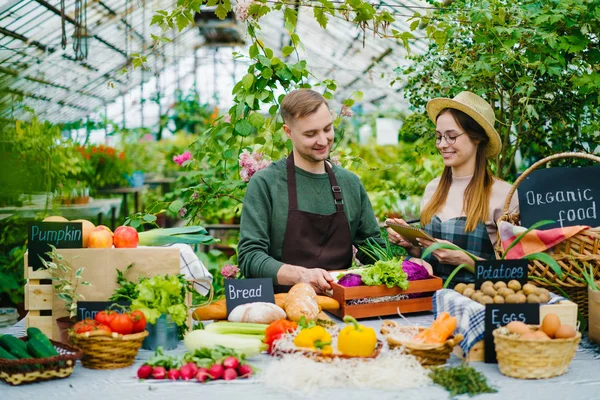 Sprzedaż ludzi mężczyzna i kobieta rozmawiają podczas ekologicznej sprzedaży żywności w szklarni — Zdjęcie stockowe