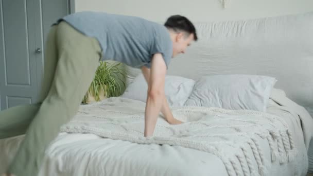 Bonito jovem saltando na cama, em seguida, deitado relaxante sorrindo no quarto — Vídeo de Stock